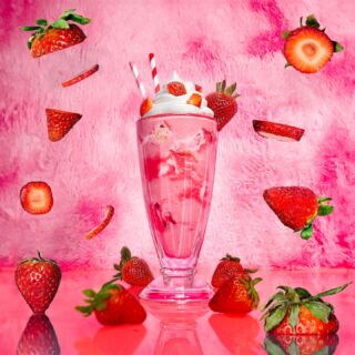 Strawberry milkshake with floating fruit slices on a vibrant pink background.